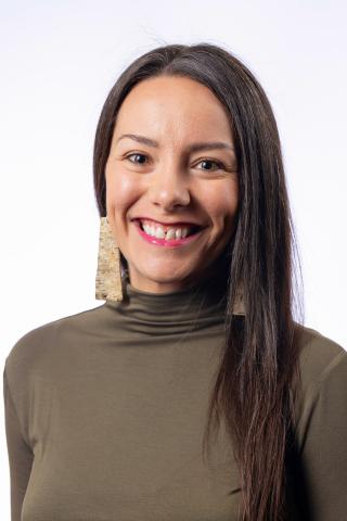 Photograph of Melissa Horner in an olive green shirt with a white background. She has long brown hair, large earrings, and is smiling. 